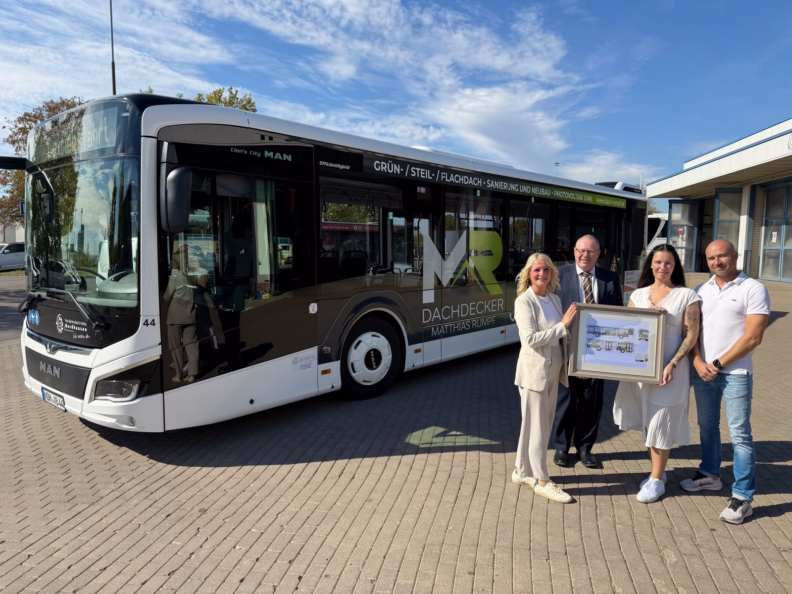 Eine Gruppe von Menschen steht vor einem weißen stadtbus mit Werbung der Dachdeckerei Rumpf