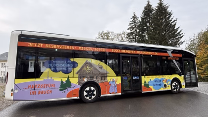 Einstiegsseite eines bunten Stadtbusses mit Werbung der Hex-Erlebniswelt