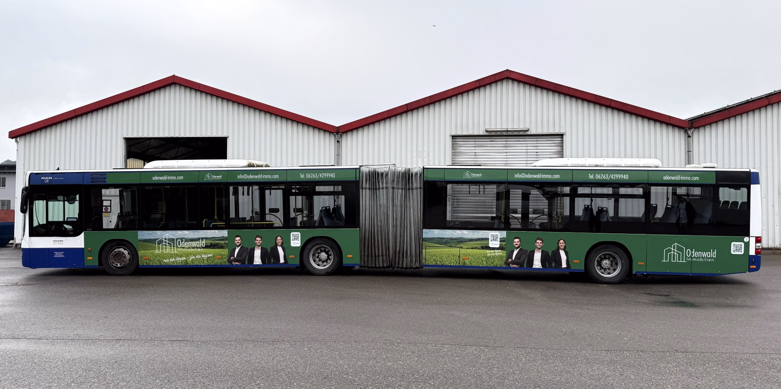 Einstiegsseite eines grünen Gelenkbusses mit Werbung der Odenwald Immobilien