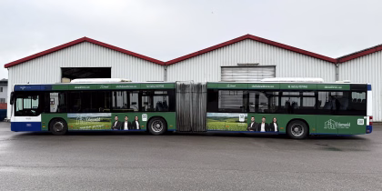 Einstiegsseite eines grünen Gelenkbusses mit Werbung der Odenwald Immobilien